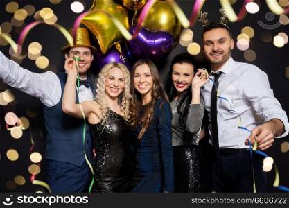 celebration, people and holidays concept - happy friends at christmas or new year party with balloons and serpentine over black background. friends at christmas or new year party