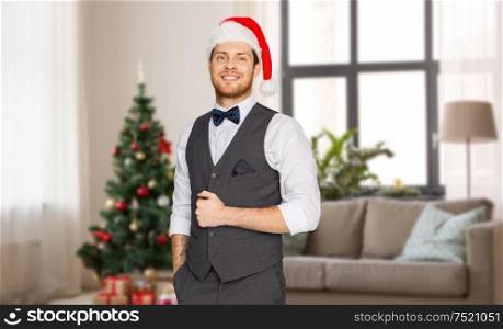 celebration, people and holidays concept - happy man in santa hat and suit over christmas tree on home background. happy man in santa hat and suit at christmas