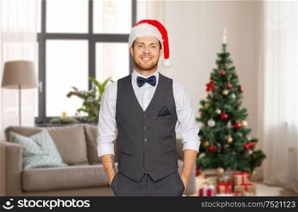 celebration, people and holidays concept - happy man in santa hat and suit over christmas tree on home background. man in santa hat and suit at home on christmas