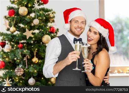 celebration, people and winter holidays concept - happy couple in santa hats with glasses of non alcoholic champagne over christmas tree on background. couple with champagne glasses at christmas party
