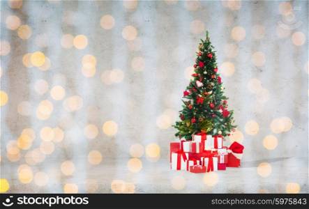 celebration, winter holidays and advertisement concept - christmas tree with gifts and santa hat over concrete wall background