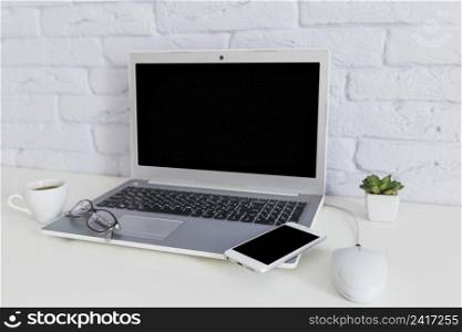 cellphone eyeglasses open laptop with coffee cup white desk