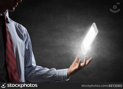 Cellphone in palm. Businessman holding in hand glowing mobile phone on dark background