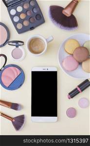 cellphone screen coffee with macaroons cosmetics products beige background