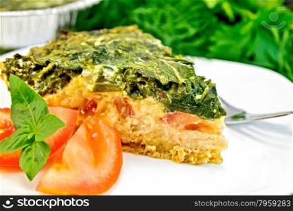 Celtic cake with spinach, tomatoes, oatmeal and eggs, a fork in the white plate and in the baking dish from a foil on a wooden boards background