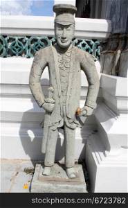 Cement sculpture of man near white temple in wat Suthat, Bangkok, Thailand