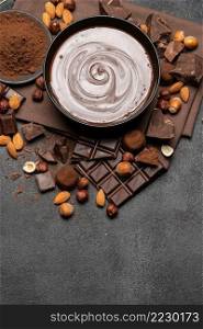 ceramic bowl of chocolate cream or melted chocolate, nuts and pieces of chocolate on dark concrete background or table. ceramic bowl of chocolate cream or melted chocolate, nuts and pieces of chocolate on dark concrete background