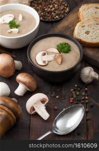 Ceramic bowl plates of creamy chestnut ch&ignon mushroom soup with spoon, pepper and kitchen cloth on dark wooden board.