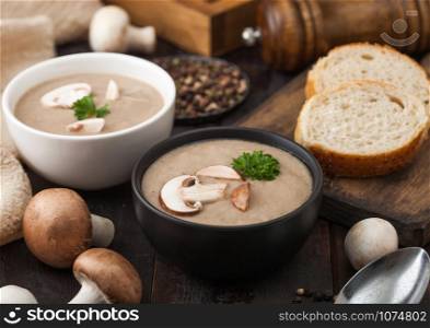Ceramic bowl plates of creamy chestnut champignon mushroom soup with spoon, pepper and kitchen cloth on dark wooden board.