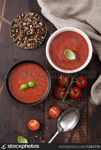 Ceramic bowl plates of creamy tomato soup with spoon, pepper and kitchen cloth on wooden board with raw tomatoes.