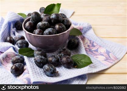 Ceramic bowl with fresh plums and blue rustic napkin on the white wooden table
