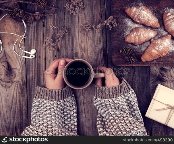 ceramic brown cup with black coffee and wooden cutting board with baked croissants, baked with icing sugar, hands holding a mug