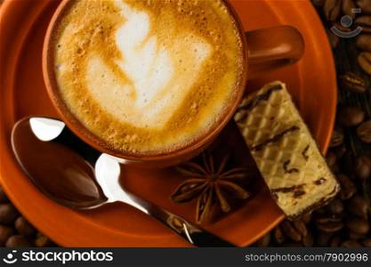 ceramic cup of cappuccino, milk-chocolate wafer and coffee beans on wooden background