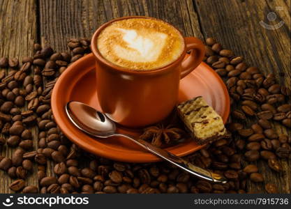 ceramic cup of cappuccino, milk-chocolate wafer and coffee beans on wooden background