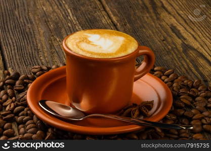 ceramic cup of cappuccino, star anise and coffee beans on wooden background