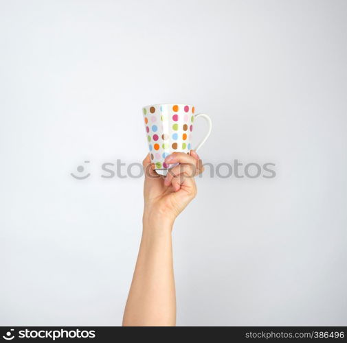 ceramic cup with multi-colored circles in a female hand on a white background, hand is raised up