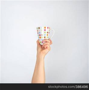 ceramic cup with multi-colored circles in a female hand on a white background, hand is raised up