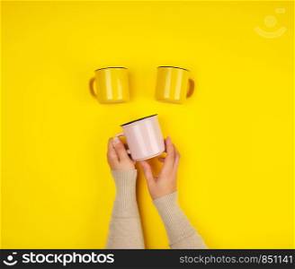 ceramic cups and female hands on a yellow background, copy space