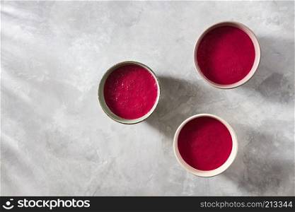 Ceramic handmade bowls with useful red smoothies for breakfast on a concrete background with shadows and space for text, flat lay. The concept of the healthy breakfasts and vegetarians. Three bowls with red beet smoothies on a concrete background, flat lay