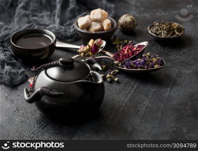 Ceramic teapot with spoons with various tea. Rose buds,blue mallow flowers,green and black loose tea and steel cup
