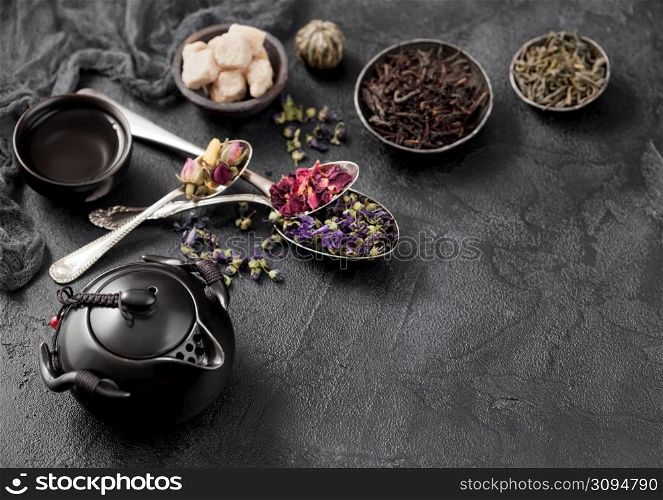Ceramic teapot with spoons with various tea. Rose buds,blue mallow flowers,green and black loose tea and steel cup