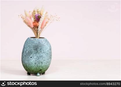 ceramic vase with bouquet of dried flowers on light brown table with pink background with copyspace