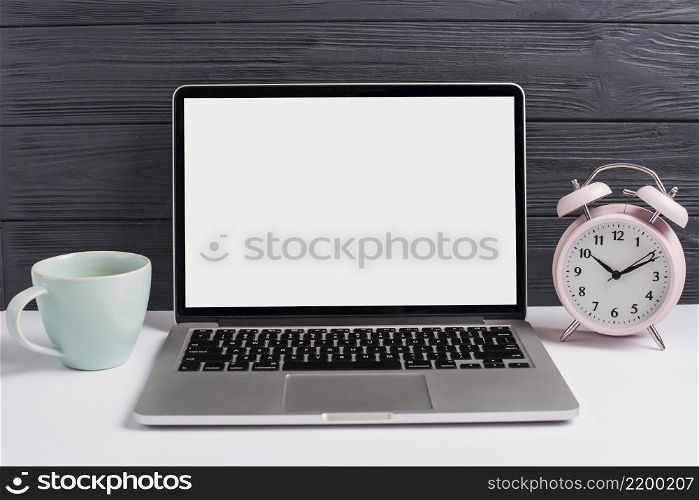 ceramics cup alarm clock open laptop white desk against wooden black background