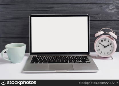 ceramics cup alarm clock open laptop white desk against wooden black background