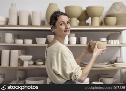 Ceramist woman holding a potter in her studio. Young female ceramist indoors holding handmade clay product. Conception of pottery