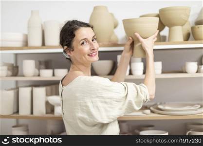 Ceramist woman holding a potter in her studio. Young female ceramist indoors holding handmade clay product. Conception of pottery