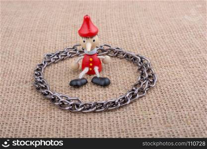 Chain around wooden Pinocchio doll sitting on canvas background