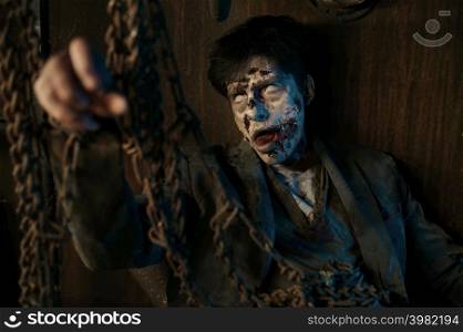 Chained zombie surrounded with candle sitting in basement of abandoned house. Mysterious nightlife. Closeup portrait. Chained zombie in basement of abandoned house