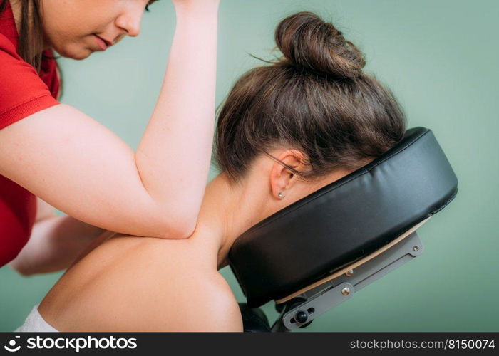 Chair Massage in the Office. Female sitting in her office on a portable massage chair. Therapist massaging her neck for stress relief