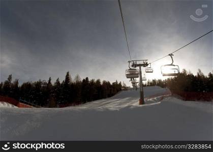 Chairlift above ski slope with sun rising behind mountain - shot in Livigno, Italian Alps