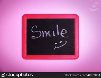 Chalkboard with an inscription smile on a pink surface, close up