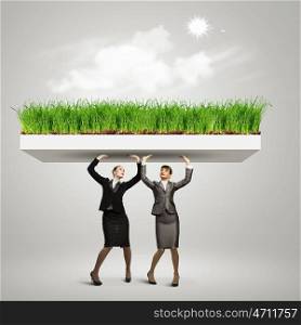 Challenge in business. Image of two businesswomen holding lawn above head. Partnership and ecology