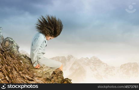 Challenge in business. Young businesswoman with waving hair sitting on top of mountain