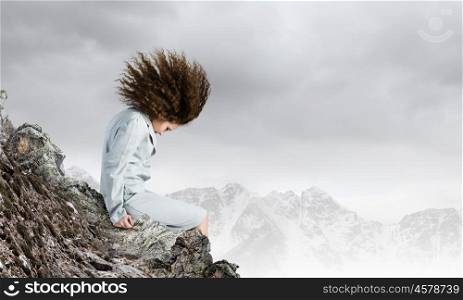 Challenge in business. Young businesswoman with waving hair sitting on top of mountain