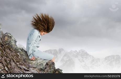 Challenge in business. Young businesswoman with waving hair sitting on top of mountain