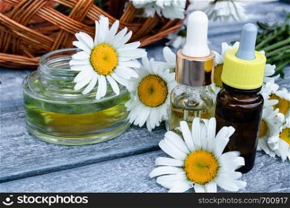 Chamomile essential oil in a glass jar and bottles near the daisies on a blue background.. Chamomile essential oil in a glass jar and a bottle near chamomile.