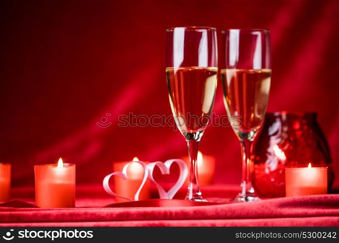 Champagne and candles. Valentines day celebration, glasses of champagne, candles and hearts on red silk