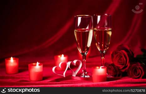 Champagne and candles. Valentines day celebration, glasses of champagne, candles, roses and hearts on red silk