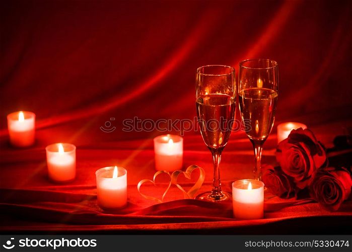 Champagne and candles. Valentines day celebration, glasses of champagne, candles, roses and hearts on red silk