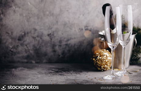 Champagne bottle in bucket with ice, glasses and Christmas decorations on concrete background