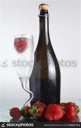 Champagne bottle with chilled class and strawberies on a wet light surface