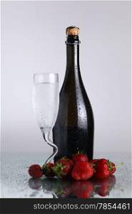 Champagne bottle with chilled class and strawberies on a wet light surface