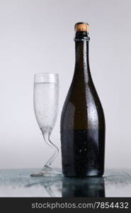 Champagne bottle with chilled class on a wet light surface