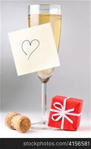 champagne glass with heart on sticky note, red gift box and cork
