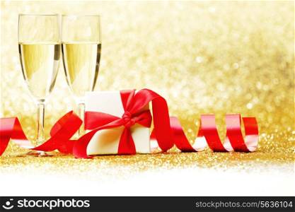 Champagne glasses and present in whitebox with red ribbon on golden background