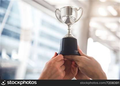 Champion silver trophy for runner up winner with sport player hands in sport stadium background. Success and achievement concept. Cup award theme. American football award and match game play prize